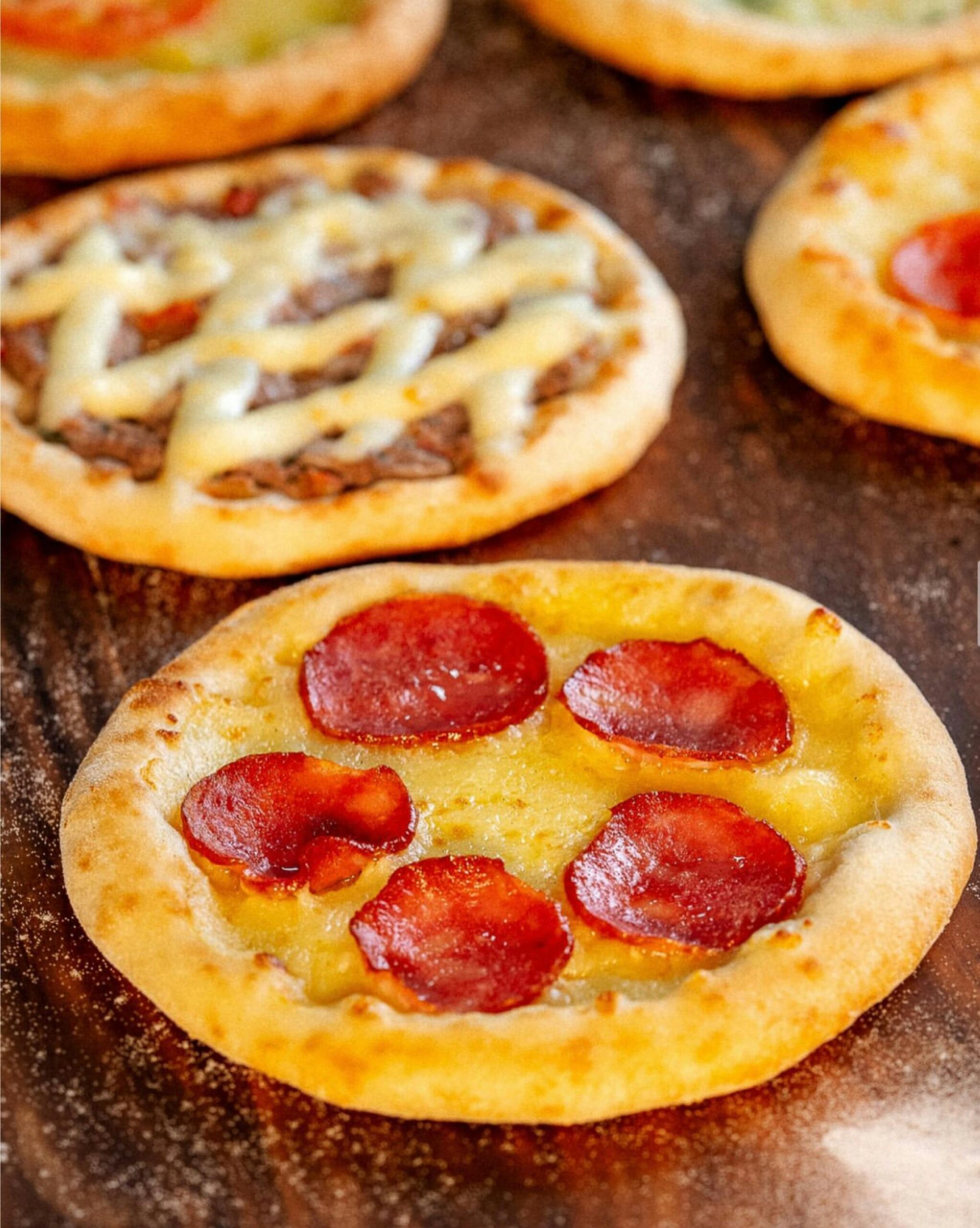 Close-up of assorted mini pizzas on a wooden surface highlighting pepperoni and cheese toppings.